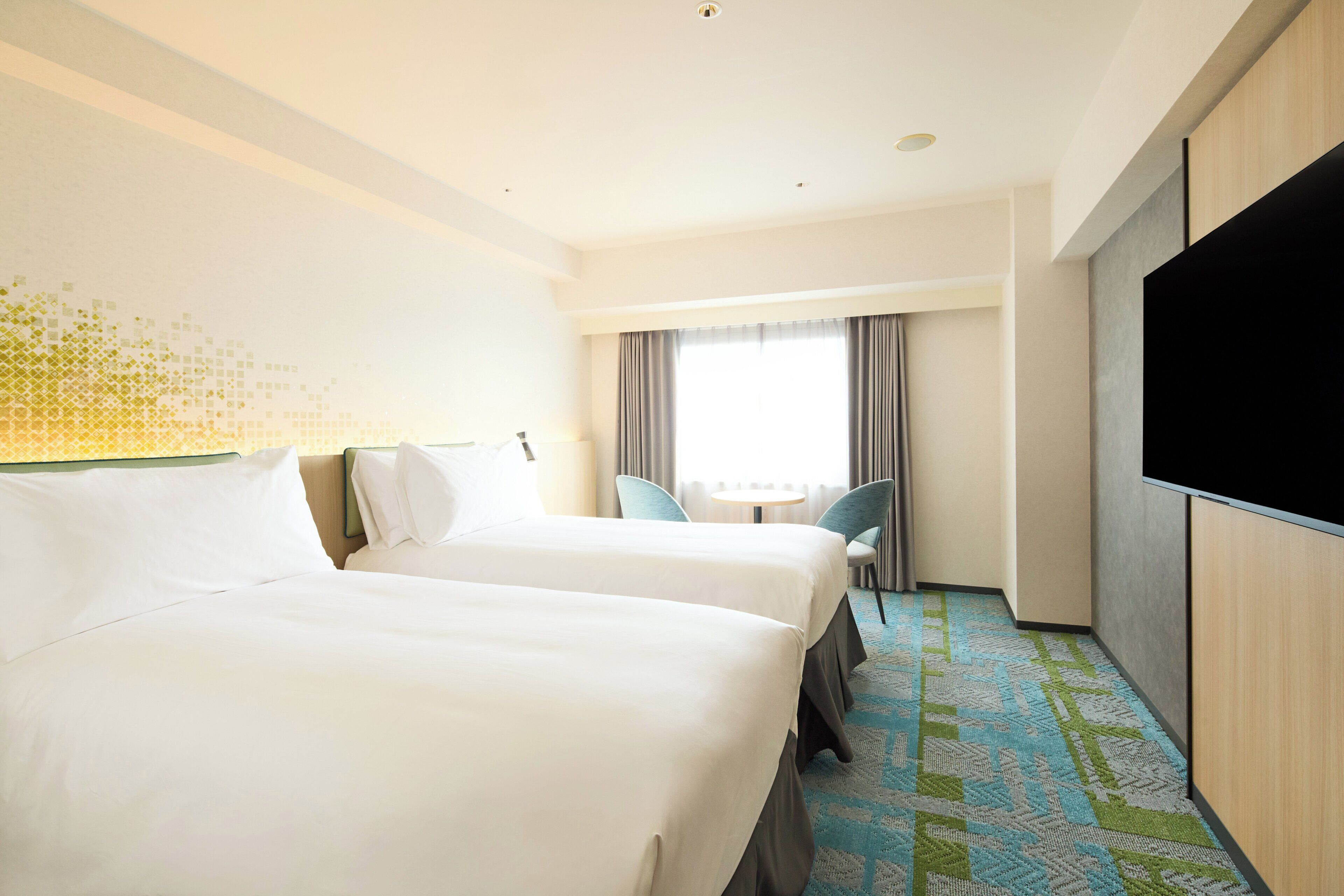 A hotel room with two beds, a TV, a desk, and a window with curtains.