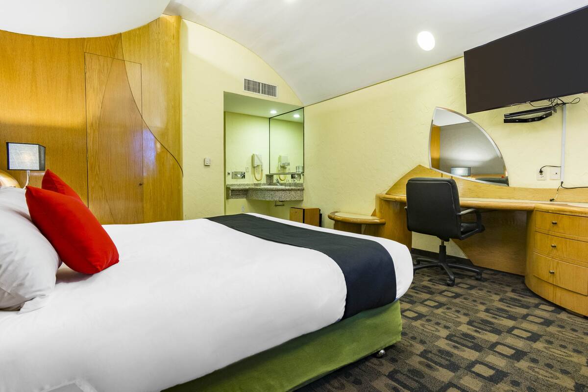 A hotel room with a bed, a desk, a chair, a mirror, and a small bathroom area.