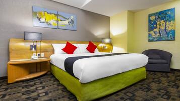 A hotel room with a large bed, two bedside tables with lamps, a chair, and two paintings on the walls.