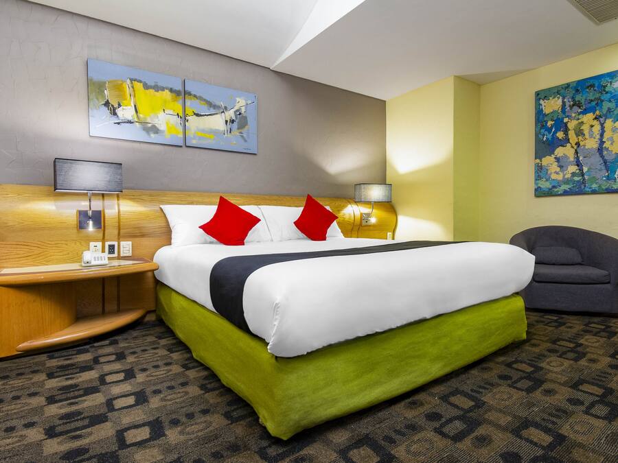 A hotel room with a large bed, two bedside tables with lamps, a chair, and two paintings on the walls.