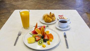A breakfast setting with a fruit plate, croissant, coffee cup, and juice glass on a table.