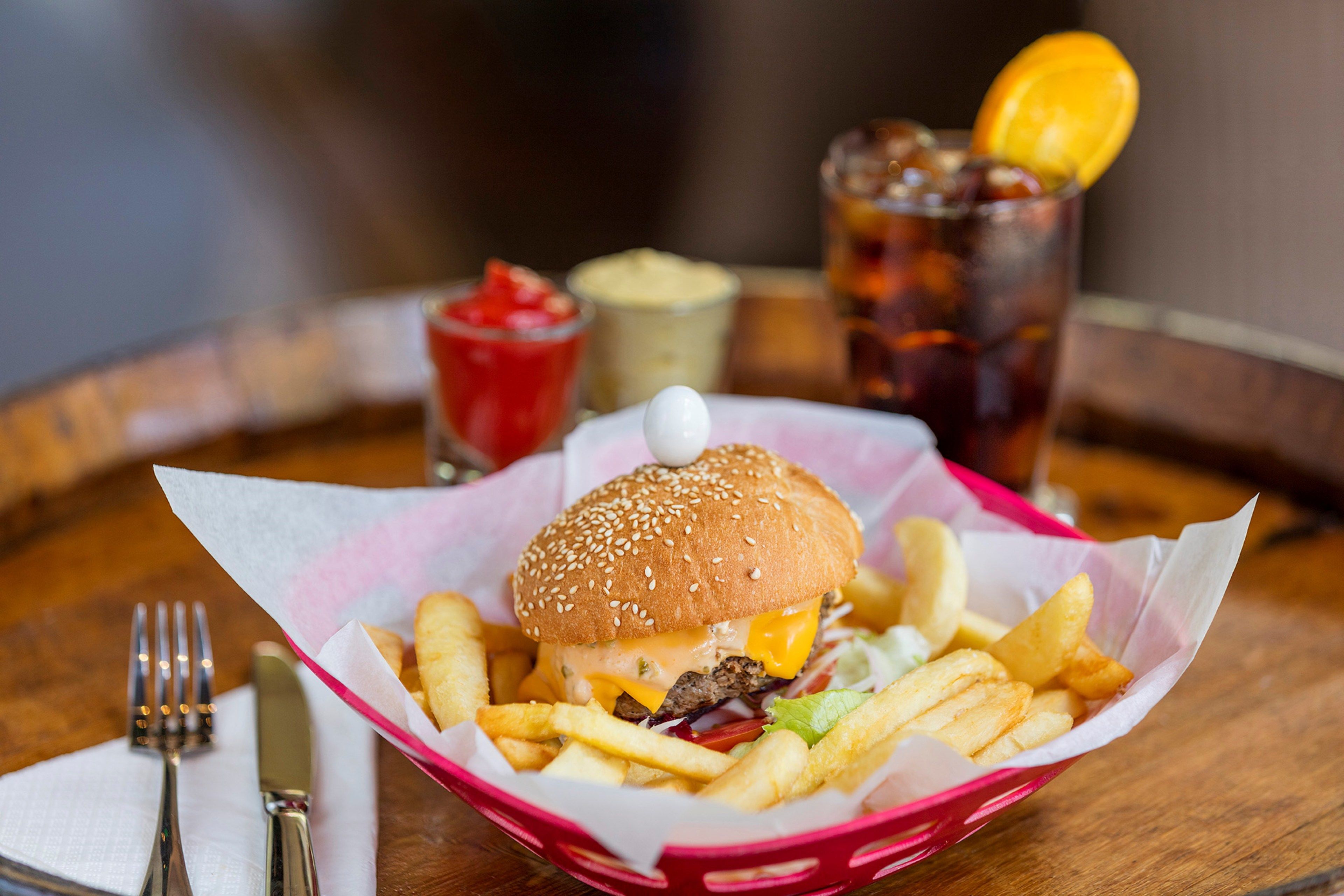 Una cesta con una hamburguesa y papas fritas sobre una mesa de madera.