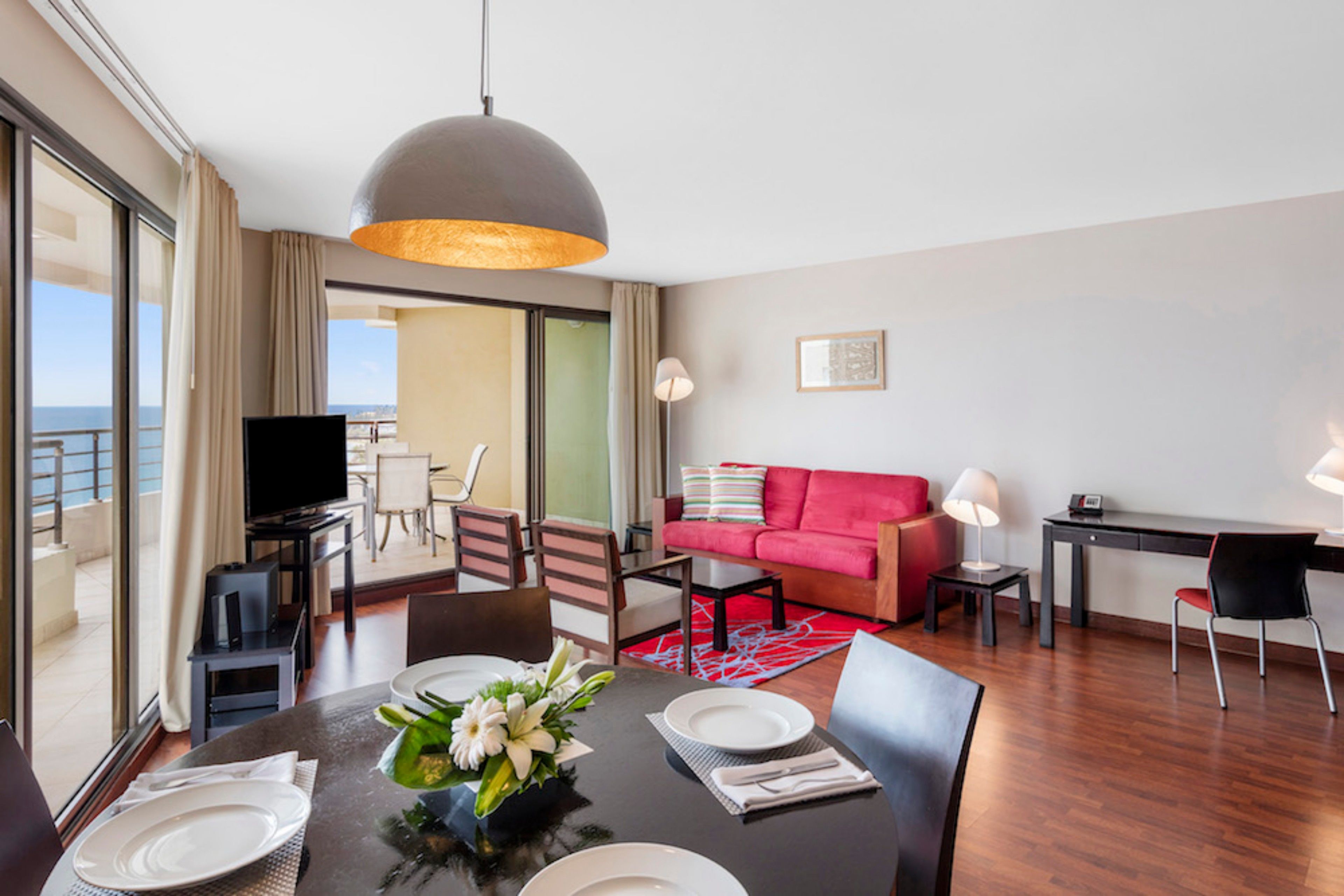 Une chambre d’hôtel moderne avec un coin repas, un canapé rouge, un bureau et un téléviseur.