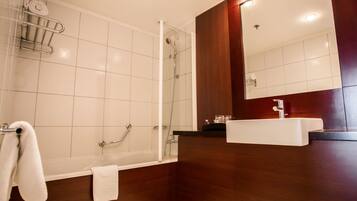 A modern bathroom with a glass-enclosed shower, a white bathtub, a wooden vanity with a sink, and a mirror.
