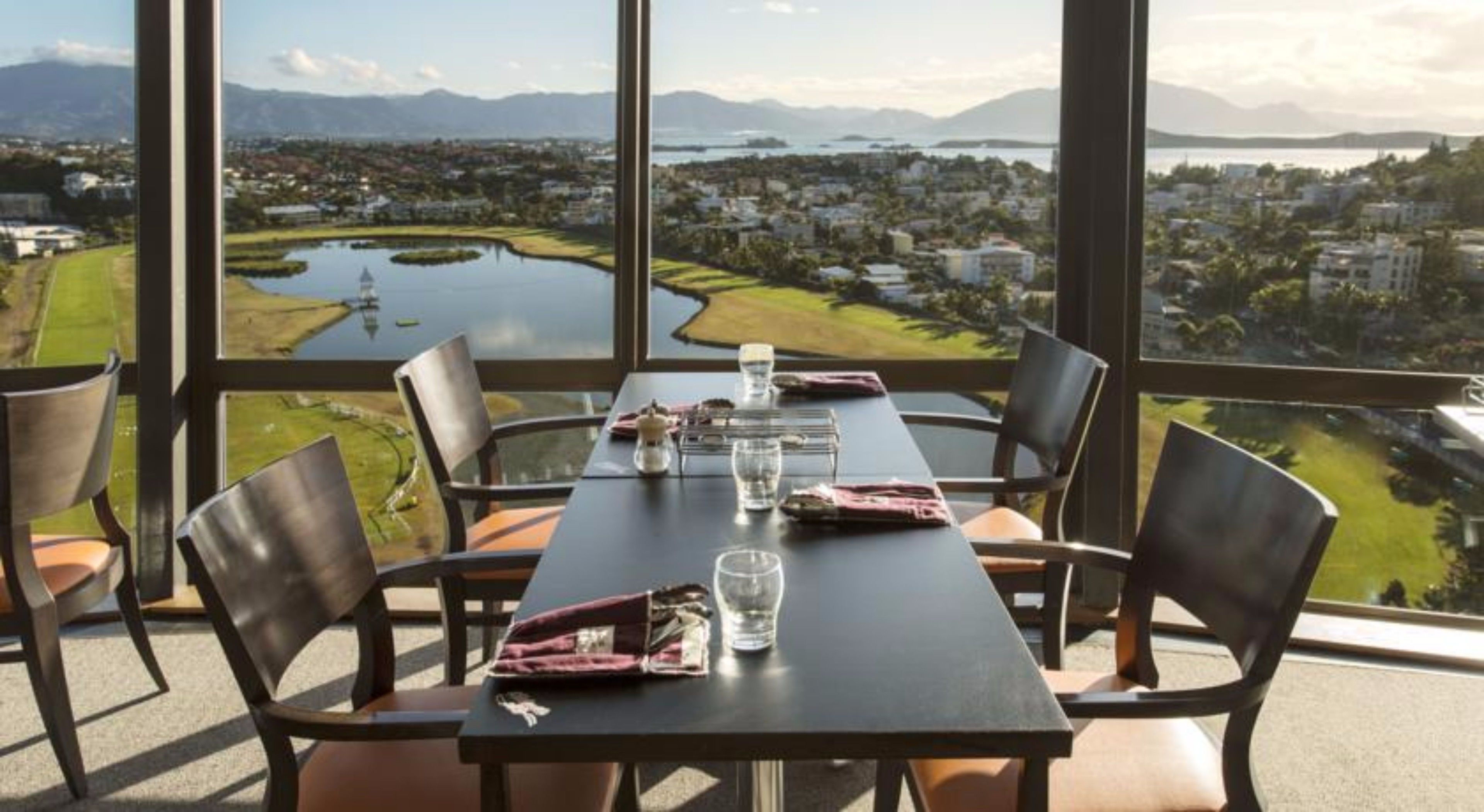 Une table à manger avec des chaises, dressée pour deux personnes, offrant une vue panoramique sur un lac et le paysage urbain.