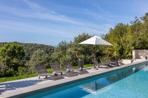 Una piscina al aire libre, sombrillas, sillones reclinables de piscina