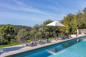 Una piscina al aire libre, sombrillas, sillones reclinables de piscina