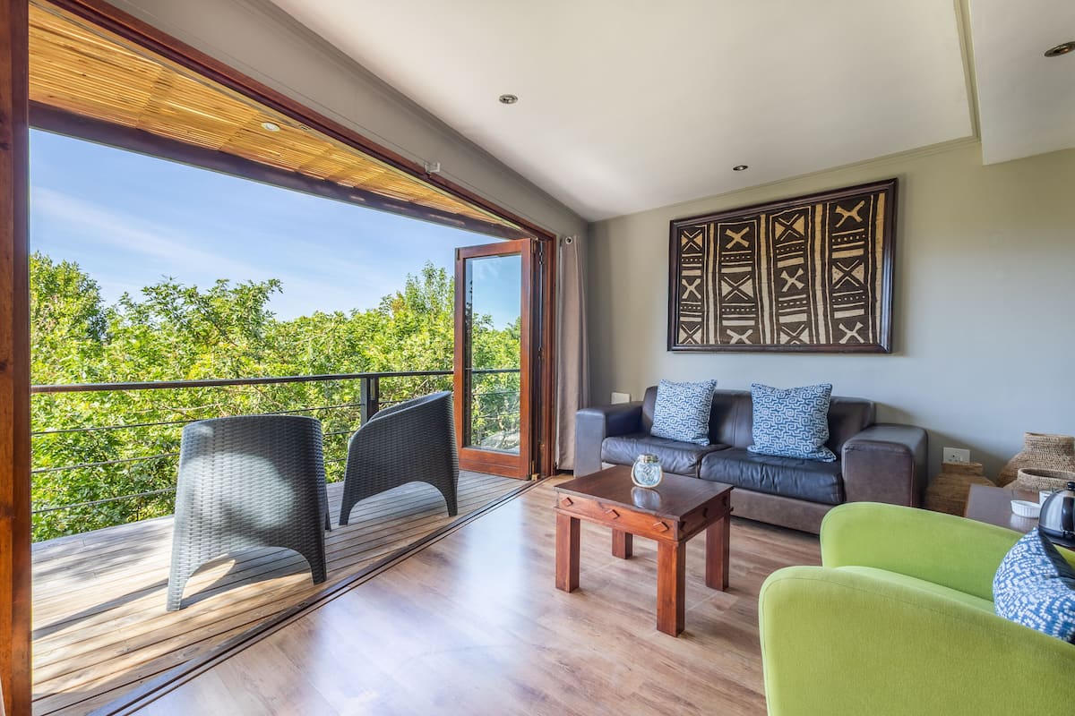 A spacious balcony with wicker chairs, a wooden table, and a sofa with patterned cushions.
