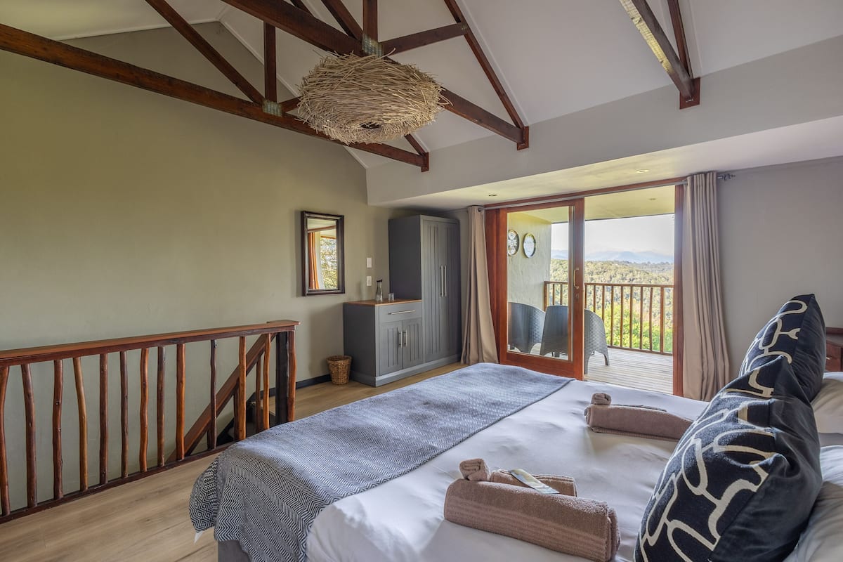 A bedroom with a large bed, a wardrobe, a balcony with a view, and a ceiling with exposed beams.