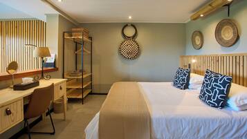 A hotel room with a bed, a desk with a lamp, a mirror, and a shelf with towels.