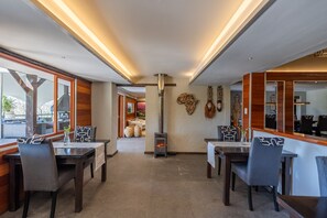 A modern dining area with wooden furniture, a central fireplace, and decorative wall art. - Hog Hollow Country Lodge (The Crags)