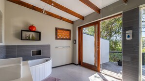 Une salle de bain moderne avec une baignoire, un plafond en bois, une porte en verre donnant sur un espace extérieur et une étagère contenant des articles de toilette.