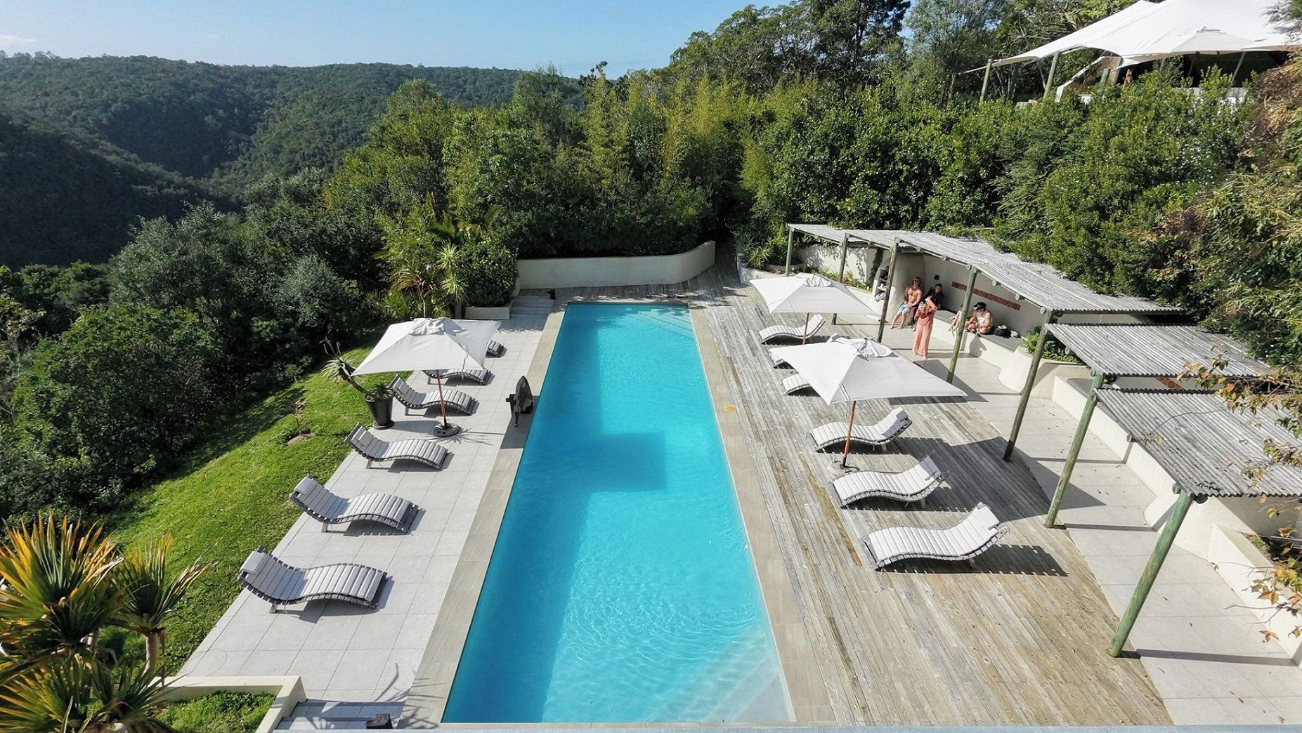 A swimming pool with lounge chairs and umbrellas, surrounded by greenery and hills.