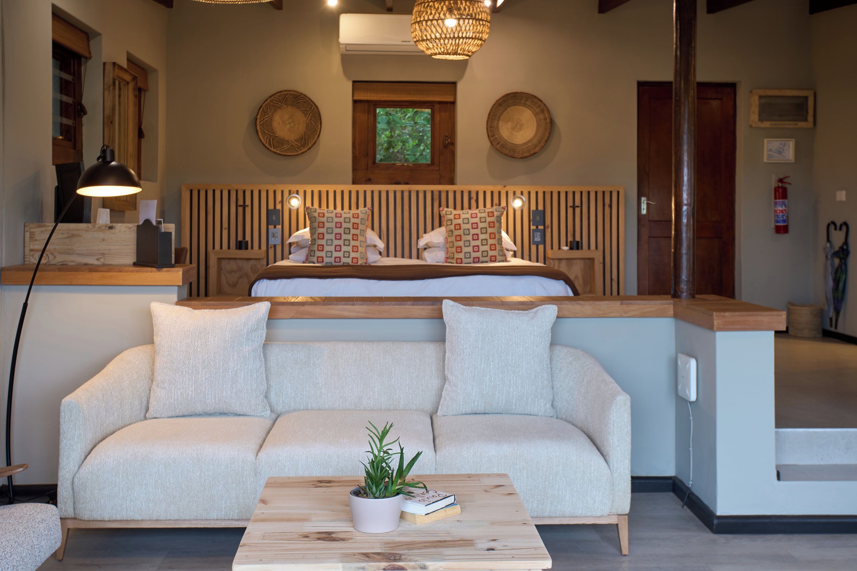 A modern bedroom with a bed, a sofa, a coffee table with a plant, and a bedside table with a lamp.