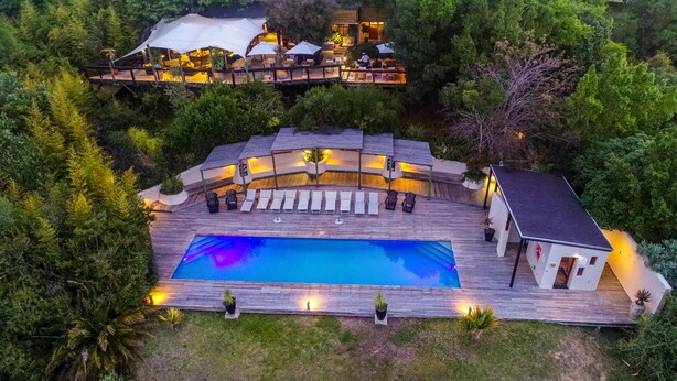 Una piscina al aire libre con sillas de descanso y una terraza, rodeada de abundante vegetación.