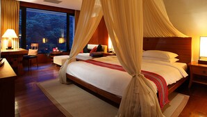A spacious bedroom with a large bed, a sitting area with a chair and table, and a view of the outdoors through large windows. - Volando Urai Spring Spa and Resort (New Taipei City)