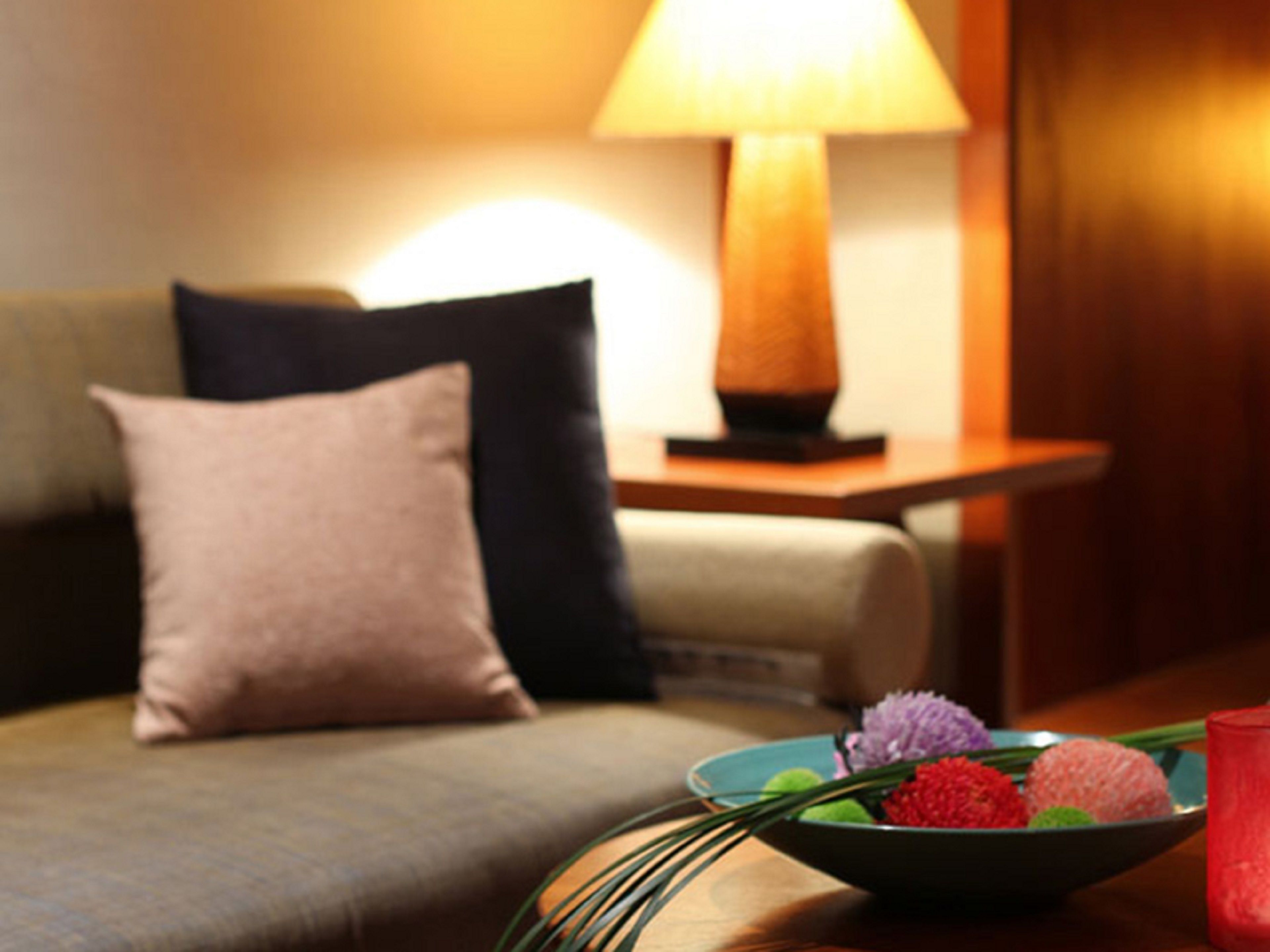 Ein Sofa mit Kissen, ein Tisch mit einer BlumenSchale und eine Lampe.
