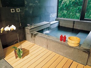 A modern bathroom with a stone bathtub, wooden flooring, and a window with a view of greenery. - Volando Urai Spring Spa and Resort (New Taipei City)