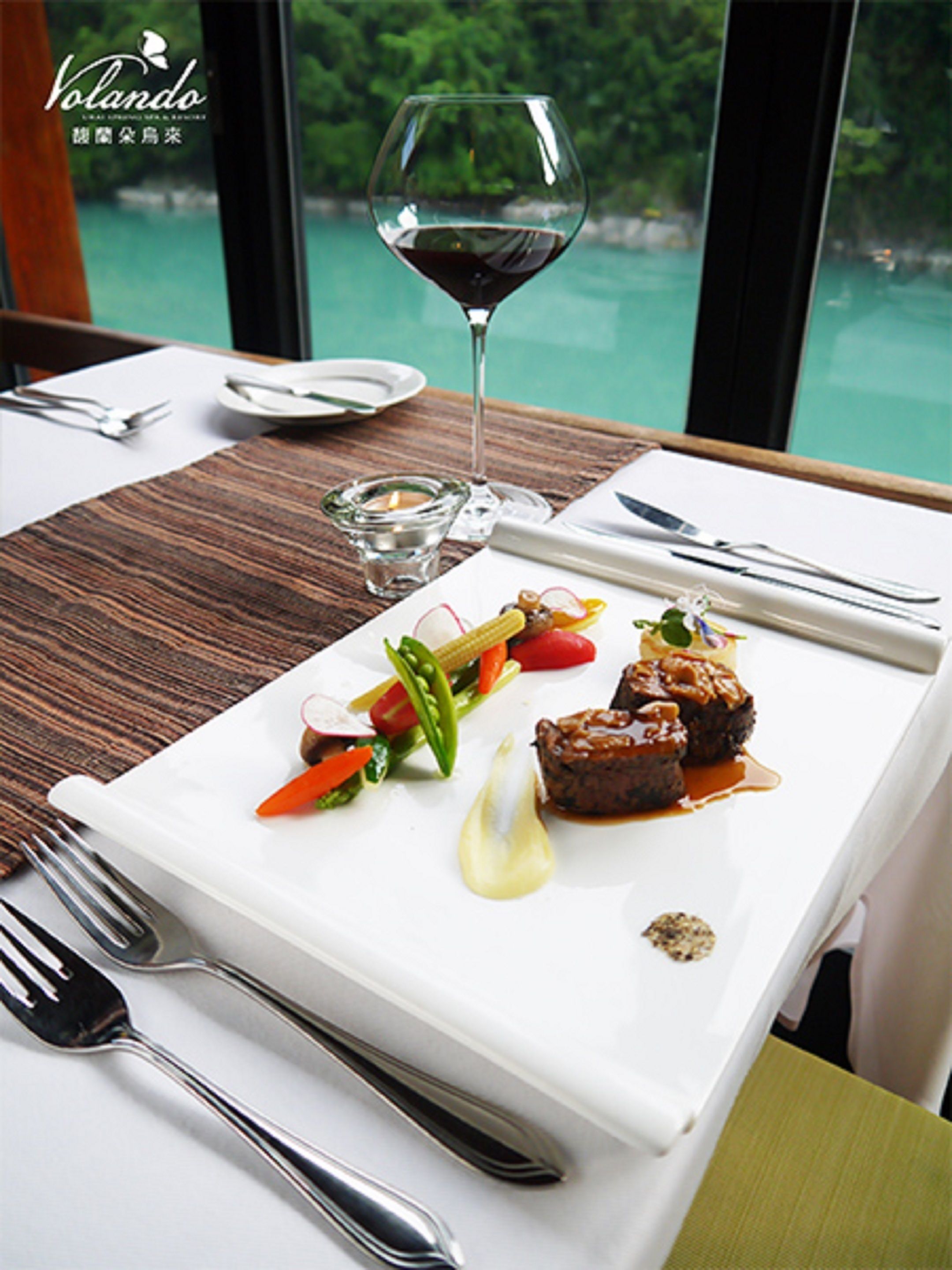 A dining table with a white plate of food, a wine glass, and cutlery.