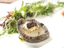 Un plato con un vieira, caviar negro y verduras.