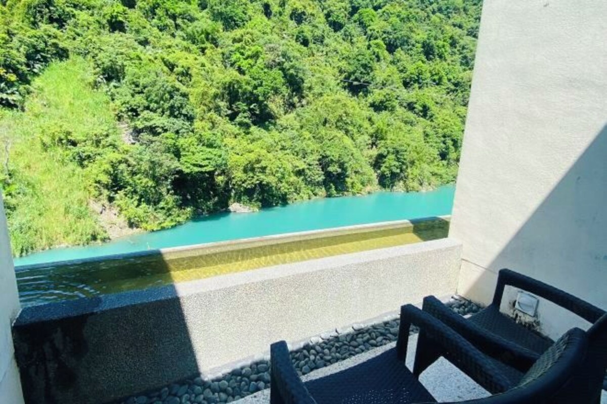 A balcony with a view of a turquoise river and dense green forest.