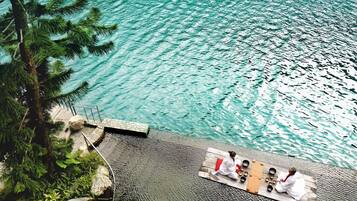 A serene outdoor setting with a wooden deck overlooking a clear body of water, surrounded by lush greenery.