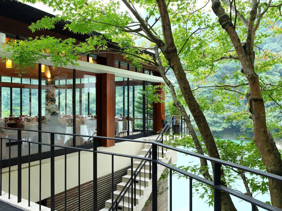 A modern building with a glass facade, wooden interior, and a view of a forested area.