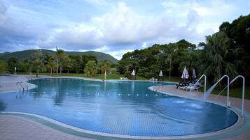 Una piscina con plataforma de baldosas, rodeada de palmeras y un paisaje montañoso.