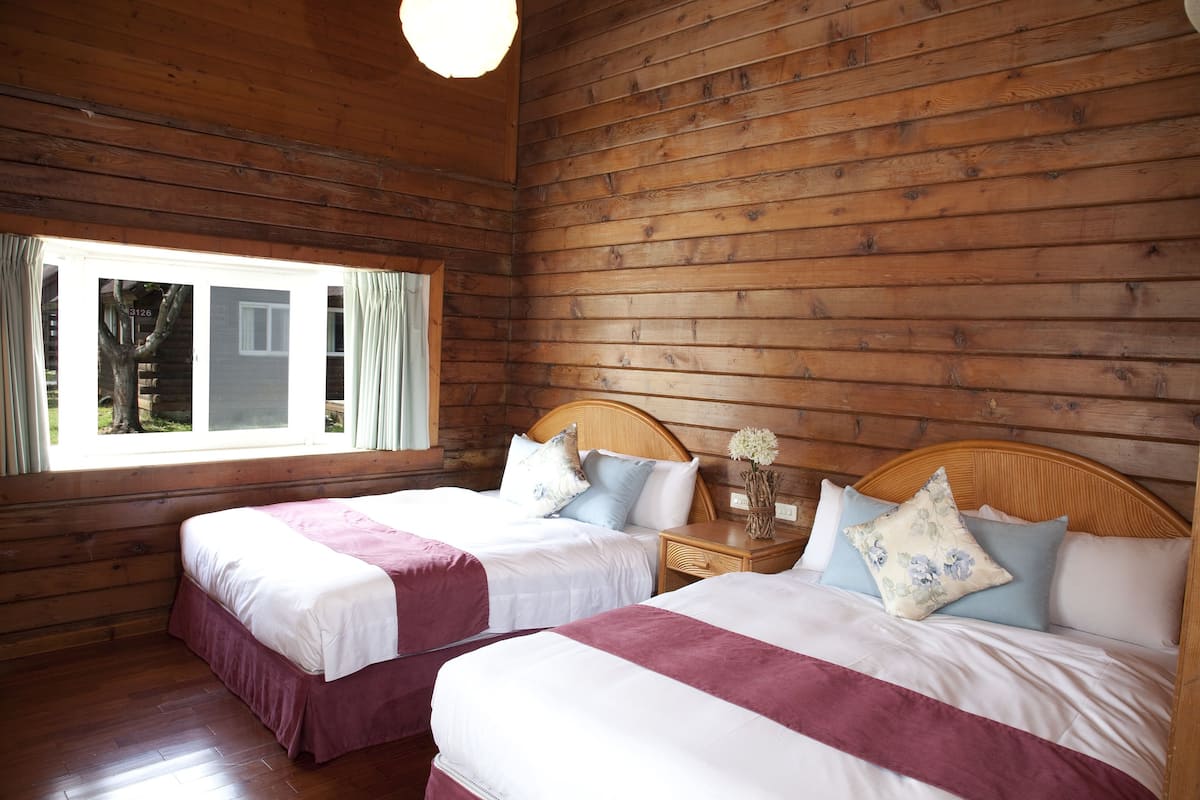 A cabin-style room with two beds, wooden walls, and a large window.
