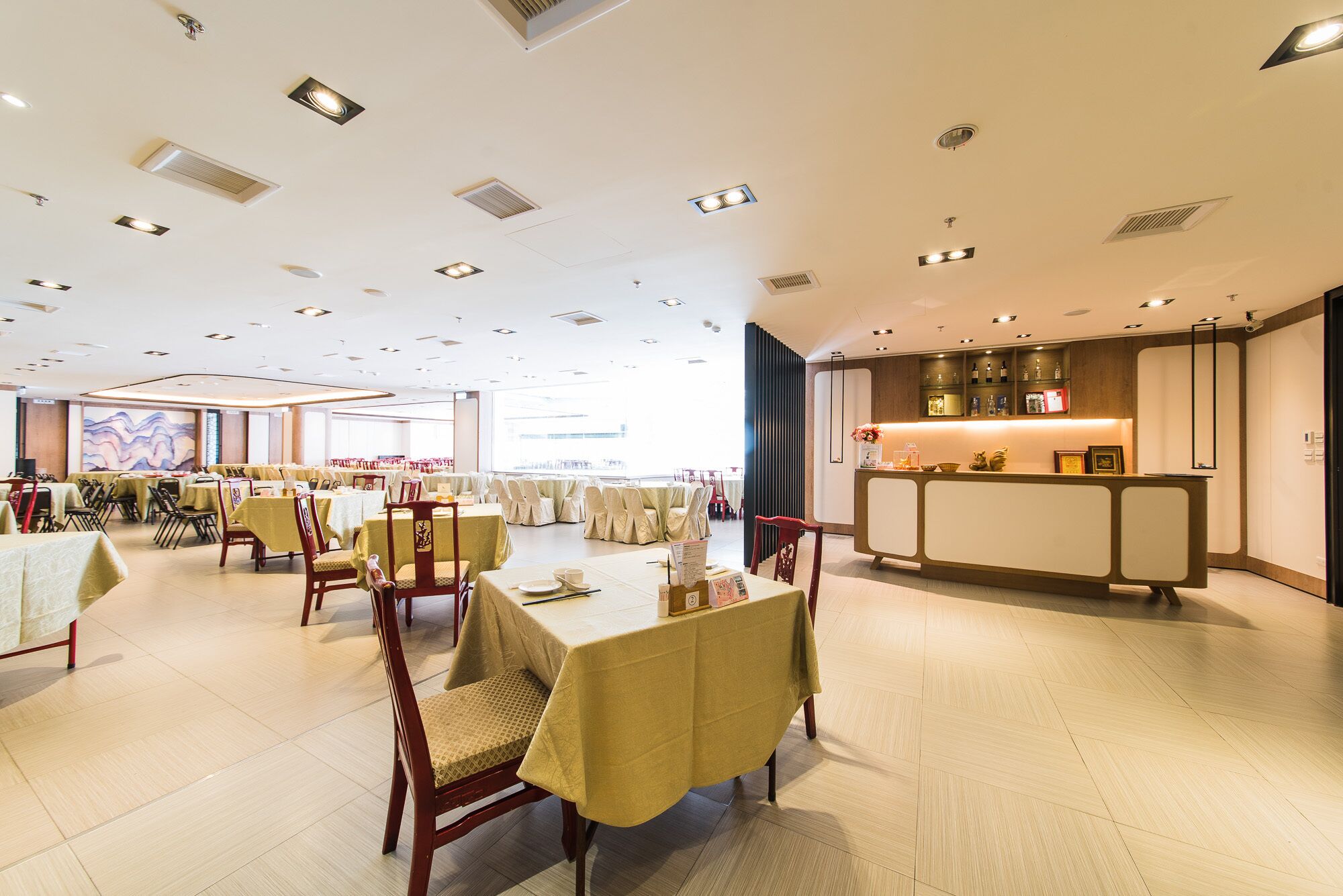 A spacious dining area with multiple tables and chairs, a reception desk, and a large window providing natural light.