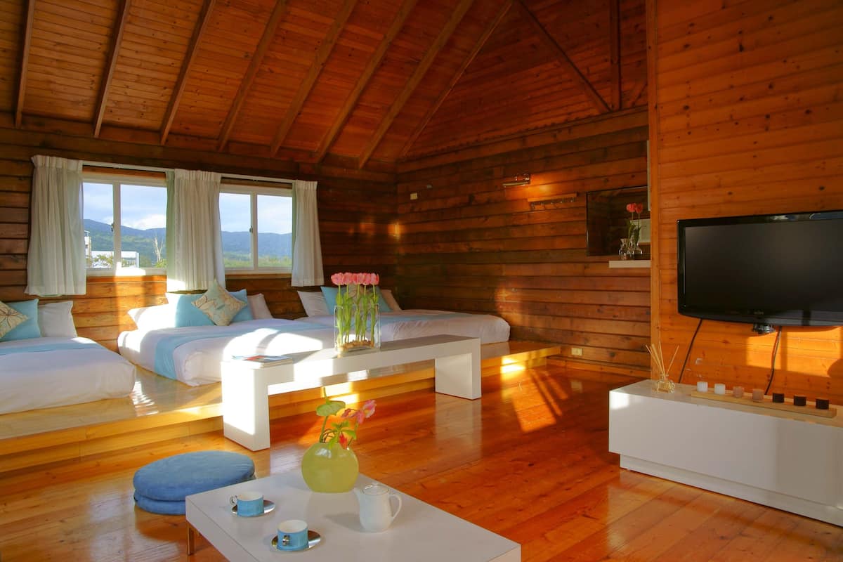 A cozy cabin with wooden walls, a large bed, a sofa, a TV, and a view of mountains through the windows.