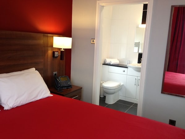 A hotel room with a bed, a bedside phone, a bathroom with a toilet and sink.