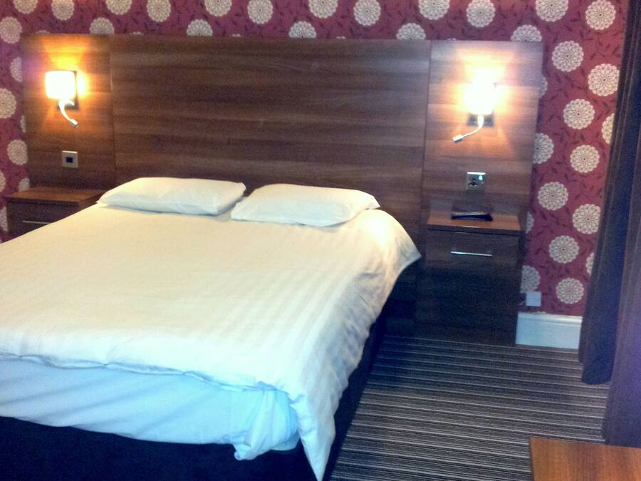 Une chambre d’hôtel avec un grand lit, deux tables de chevet et des lampes fixées au mur.
