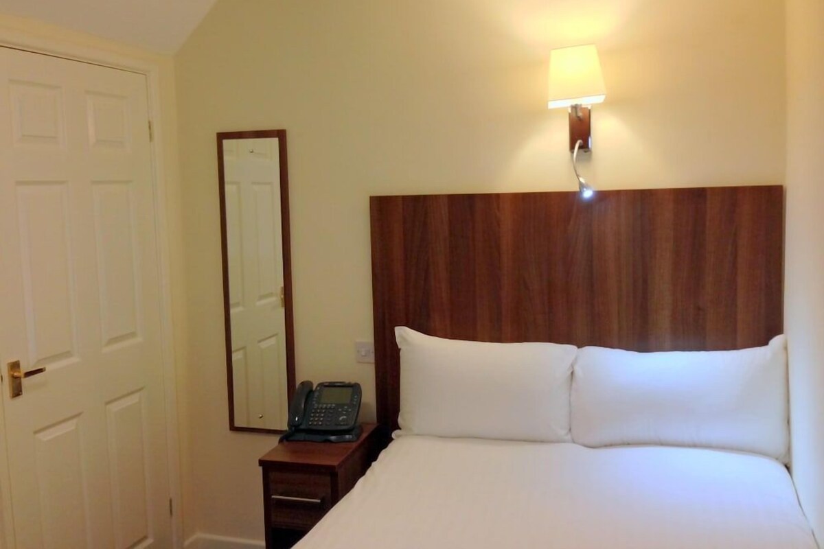 A hotel room with a wooden headboard, a bedside telephone, and a wall-mounted light fixture.