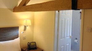 A hotel room with a wooden ceiling, a bed, a bedside table with a lamp, and a telephone. - Ely House Hotel (Wolverhampton)
