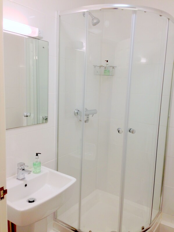 A modern bathroom with a glass-enclosed shower, a white sink with a soap dispenser, and a mirror above the sink. - Ely House Hotel (Wolverhampton)