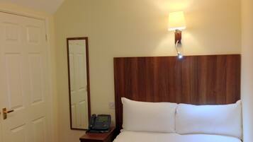 Ein Hotelzimmer mit einem Holzkopfteil, einem Nachttisch mit Telefon und einer Wandleuchte sowie einer Tür.