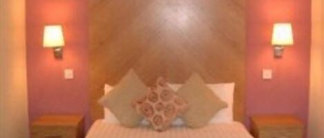Un dormitorio con cabecera de madera, dos mesitas de noche y una colcha estampada.