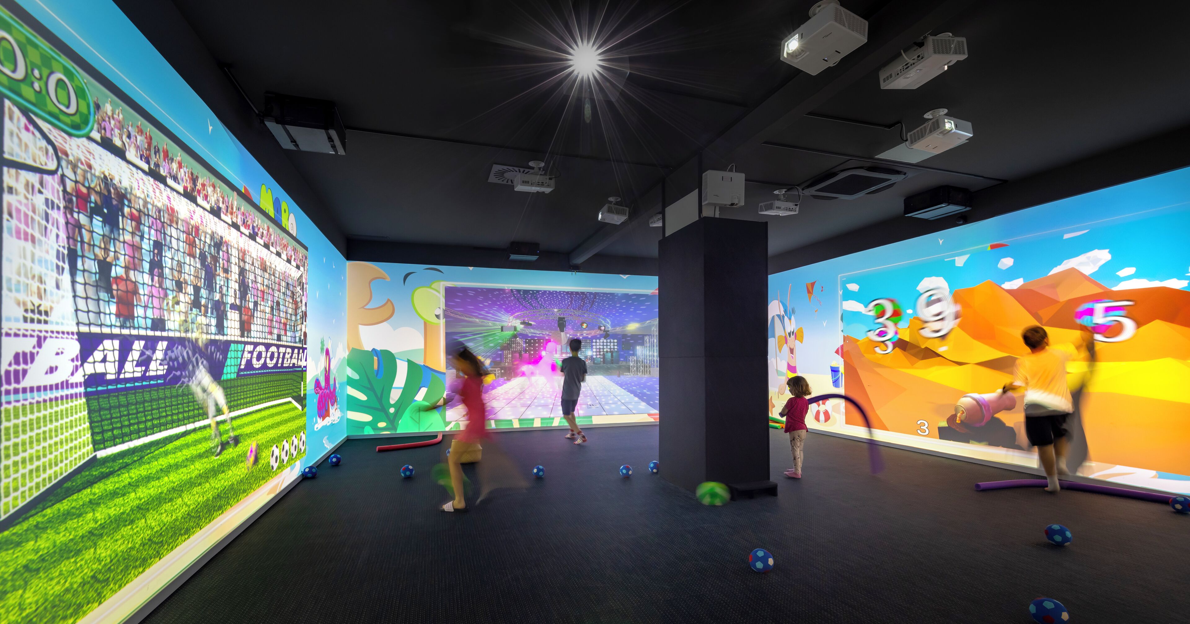 Espaço de recreação infantil em ambiente interno, com telas interativas e diversos brinquedos.