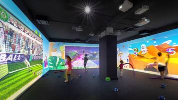 Espaço de recreação infantil em ambiente interno, com telas interativas e diversos brinquedos.