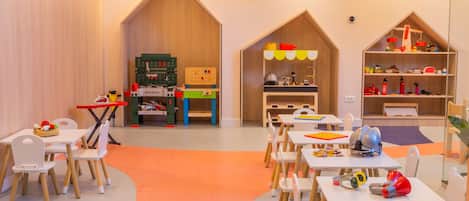 Une salle de jeux pour enfants avec des tables, des chaises et des jouets éducatifs.