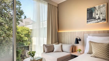 Una habitación de hotel moderna con un balcón grande, un sofá, una mesita de noche, una lámpara y una cama.