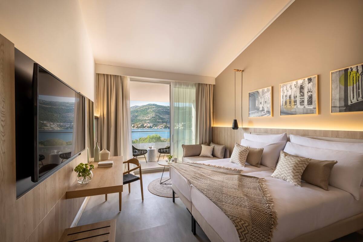 A modern hotel room with a large bed, a desk, and a view of the sea.
