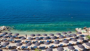 A beach with rows of sun loungers and umbrellas, clear blue water, and rocky outcrops. - Valamar Tirena Hotel (Dubrovnik)