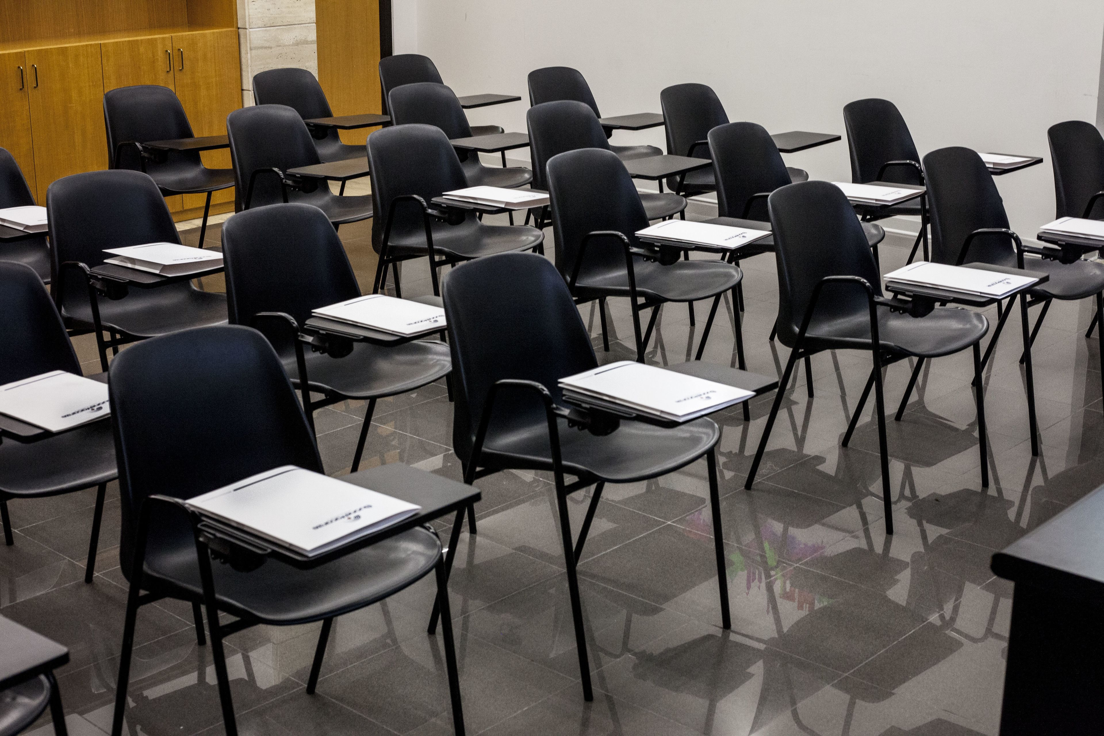 Un aula con filas de sillas y pupitres negros, algunos con cuadernos.