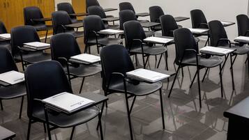 Un aula con filas de sillas y pupitres negros, algunos con cuadernos.