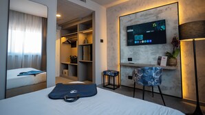Habitación de hotel con cama, escritorio, monitor de computadora, silla, taburete pequeño y armario.