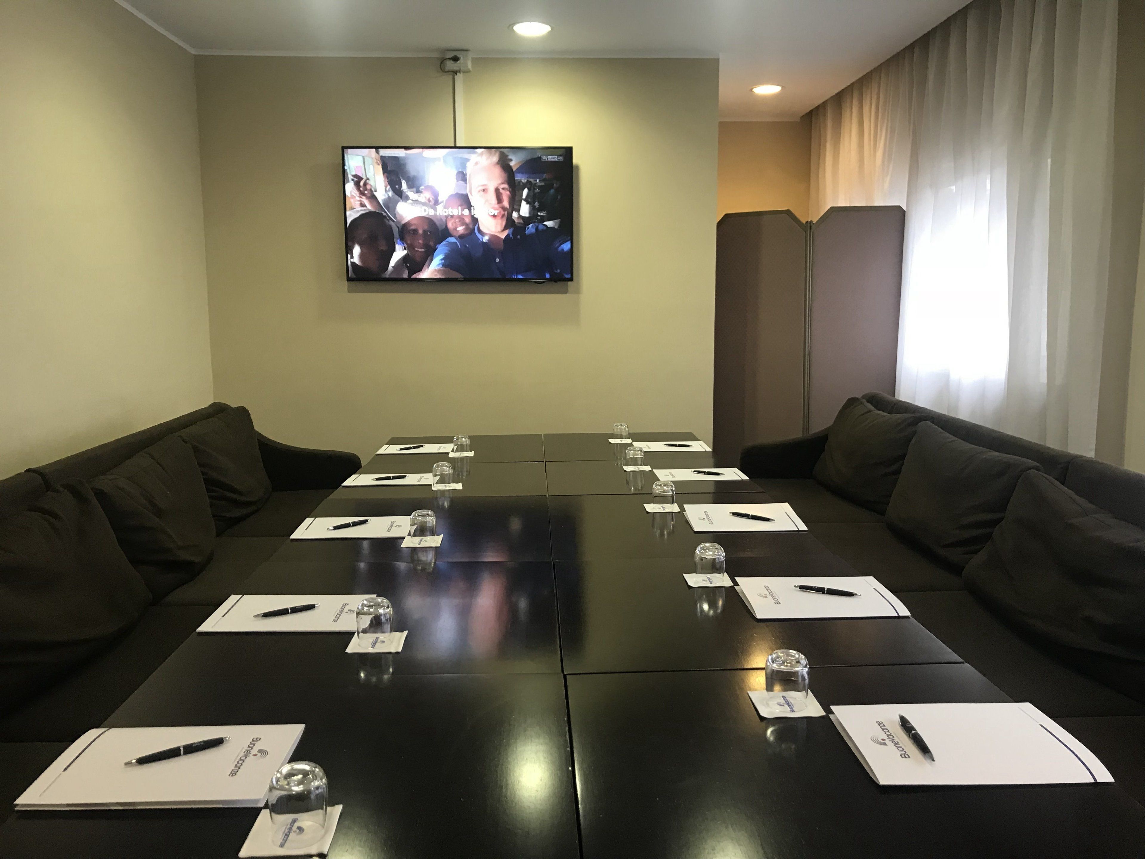 Una sala conferenze con un lungo tavolo, divani in pelle nera e una TV a parete.