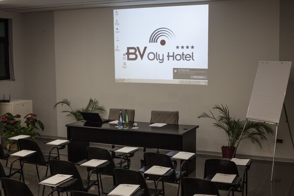 A conference room with a large screen displaying the BVoly Hotel logo, a black conference table, and several chairs.