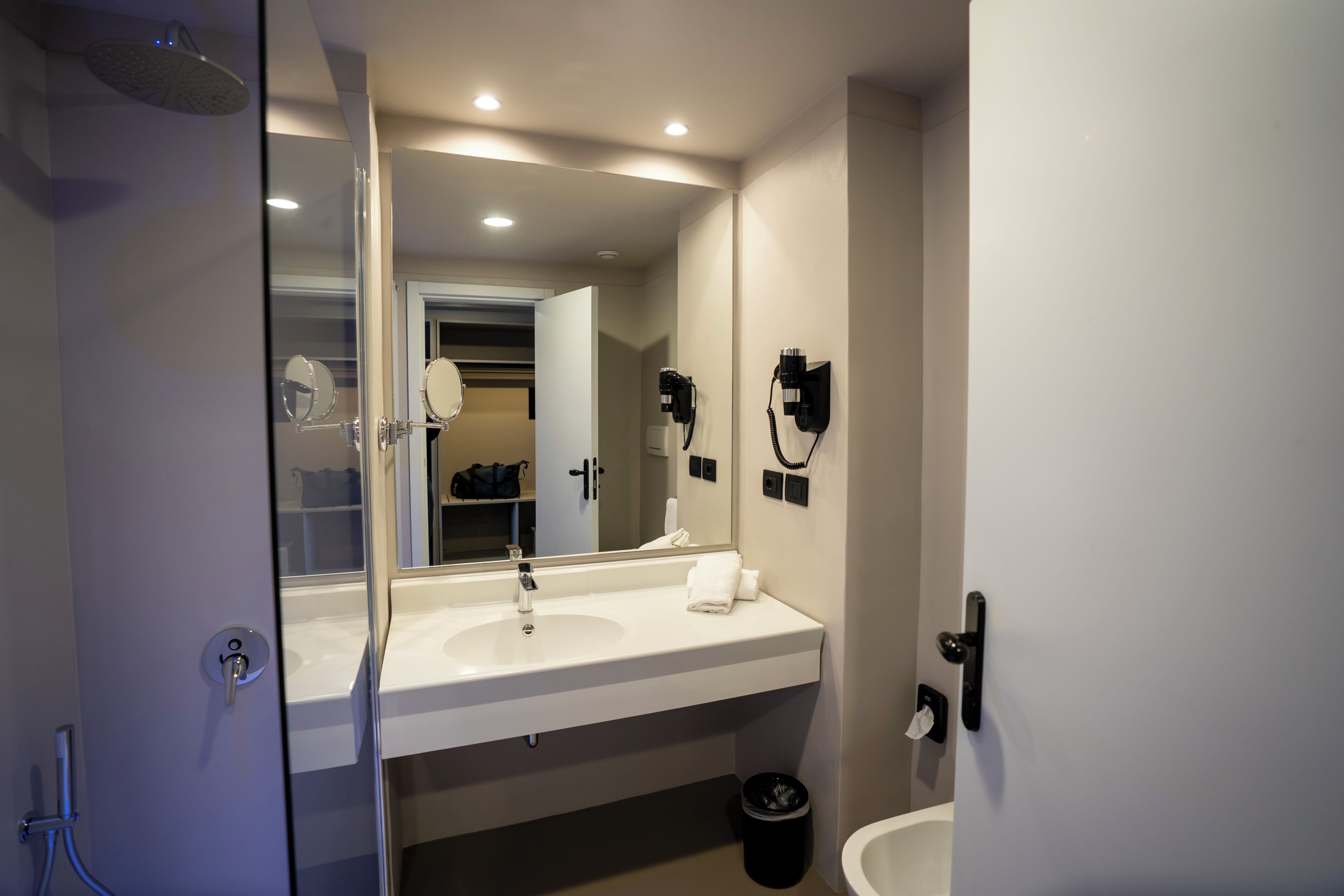 Une salle de bain moderne avec un grand miroir, un lavabo blanc et une douche.